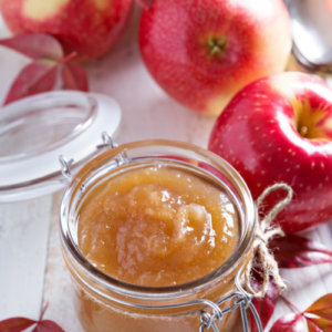 homemade apple butter in a jar surrounded by apples