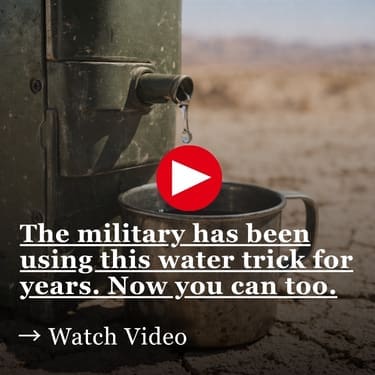A weathered military-green metal device with a small spout dripping clear water into a dented metal cup, sitting on dry cracked desert ground with a barren landscape in the background
