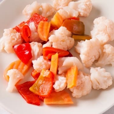 A white plate with pickled cauliflower florets, sliced red bell peppers, orange carrots, and green pepper pieces, viewed from above.